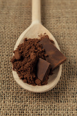 Cocoa powder with a few pieces of chocolate in wooden spoon on burlap napkin