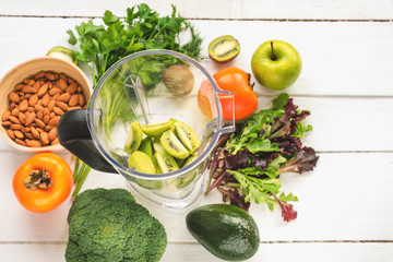 Ingredients for detox smoothies in a blender: apples, kiwi, avocado, persimmon, lettuce, broccoli, almonds, dill and parsley on wooden table. Top view.