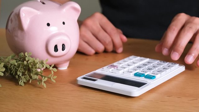  ピンクの豚の貯金箱と電卓で計算する男性
