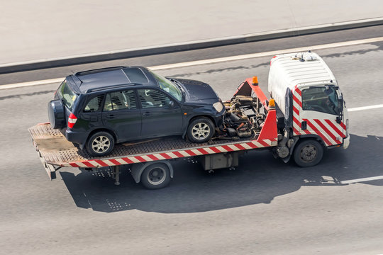 Tow truck carries an evacuated car on a highway, aerial view.