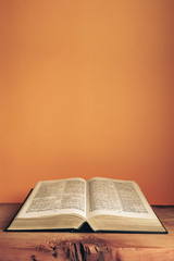 Fototapeta na wymiar Open Holy Bible on a old wooden table. Beautiful orange wall background..