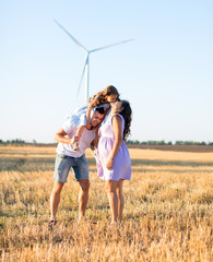 young husband, pregnant wife kissing daughter on the father's shoulders on the field, wind turbines on the background