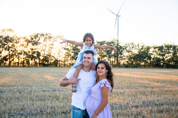 happy young husband, pregnant wife and a little girl on the father's shoulders on the field, wind...