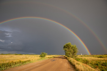 Cumulonimbus clouds, torrential rain and double rainbow over the steppe road. Akmola Region, Kazakhstan.