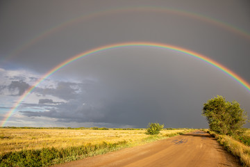 Cumulonimbus clouds, torrential rain and double rainbow over the steppe road. Akmola Region, Kazakhstan.