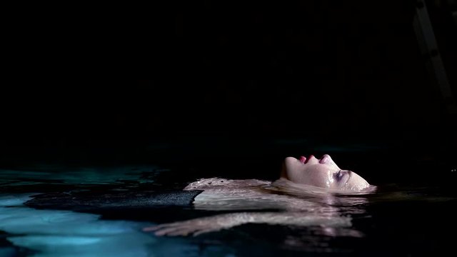 beautiful woman is floating in pool face up in night, dressed in gown