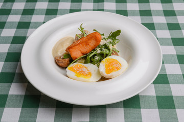 Grilled red fish steak and boiled eggs served in a white plate over green plaid tablecloth. Italian cuisine, concept.