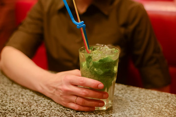 Person drinking Mojito cocktail sitting at table in cafe or restaurant or bar. Leisure time.