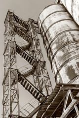 Old, abandoned concrete plant with iron rusty tanks and metal structures. The crisis, the fall of the economy, stop production capacity led to the collapse. Global catastrophe. Old photo effect