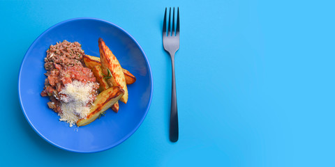 Baked potatoes with mushroom stew topped with melted cheese in a blue bowl. Served over blue background.
