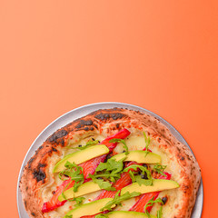 Close-up of a delicious smoked salmon pizza with cheese, avocado and smoked salmon. Sea-food. Orange background.