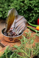 Dried beef ears in the dog vessel among the greenery on the wooden board. Chewing treats for domestic dogs. Natural dental treats for promotion and pampering.
