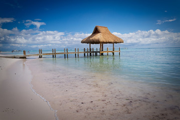 Tropical white sandy beach. Palm leaf roofed wooden pier with gazebo on the beach. Punta Cana, Dominican Republic