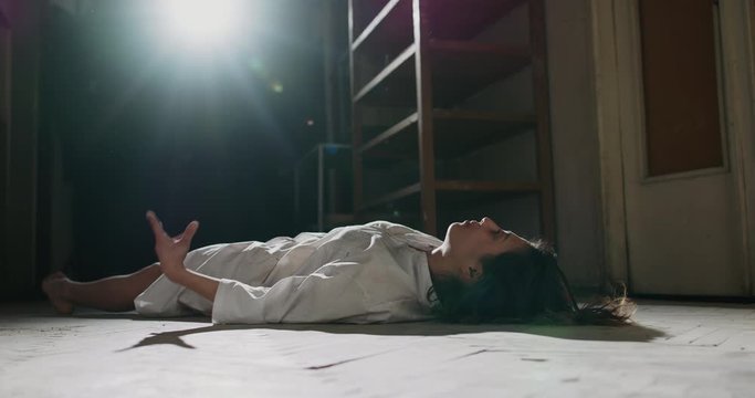 Exhorcist girl in white shirt convulsing on old wooden floor. Scary female demon awakening in haunted hallway - halloween costume, horror movie 4k footage