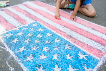 Two cute friends girls drawing American flag with colored chalks on the sidewalk near the house on sunny summer day. Kids painting outside. Creative development of children. Patriotic day concept