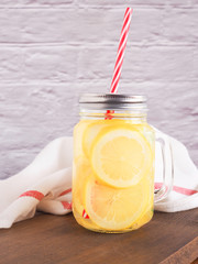 Fresh lemons slice in mason jar with straw on cutting board  with a backdrop of fabric. and grey wall. Space for your text. Drink for detox, and refresh the body..