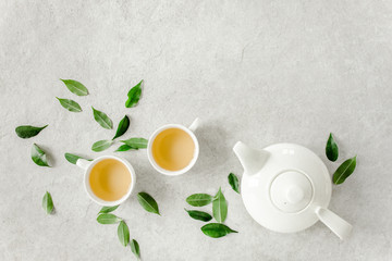 Herbal tea with two white tea cups and teapot, with green tea leaves. Flat lay, top view. Tea concept