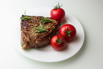grilled steak with vegetables on a white plate, seasoned with pepper and rosemary, close-up