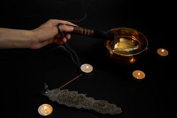 close up of a girl holding a singing bowl pestle on a black background. incense sticks