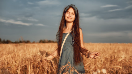 Obraz premium Portrait of Little girl 10-12 years old with long brown hair, walk in a wheat field on a summer evening