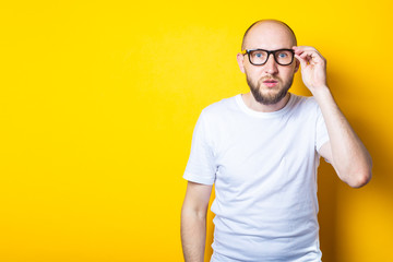 Serious bearded bald young guy with glasses on yellow background.