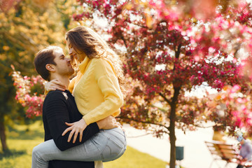 Fototapeta premium Cute couple in a park. Man in a black jacket. People walks. Couple near blooming trees