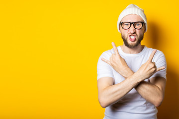 Fototapeta premium Bearded young man with crossed arms shows a rocker goat gesture on a yellow background