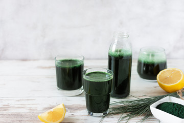 Spirulina drink with lemon and spirulina algae powder on white wooden table.