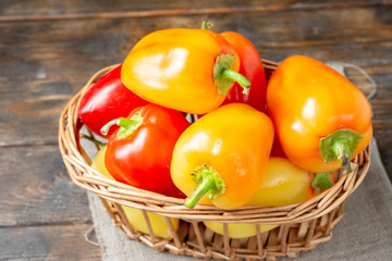 Sweet pepper. Red, yellow and orange peppers in a basket on a brown wooden table. Paprika close up