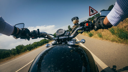 Driving a black old motorbike with wide handlebar on an asphalt road under a blue sunny sky