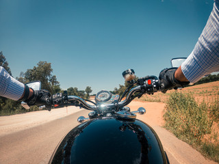 Driving a black old motorbike with wide handlebar on an asphalt road under a blue sunny sky