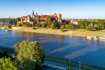 Fototapeta premium Royal Wawel Cathedral and castle in Krakow, Poland. Aerial view in sunset light. Vistula River, tourist boats, canoes, riverbanks with trees, parks, promenade and walking people