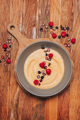 Keto plain porridge placed on a wooden serving board and wooden table with some raspberries and dried black berries