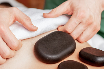 Obraz na płótnie Canvas Young man receiving a stone massage on back while hands of massage therapist puts stones on her back.