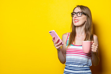 Young woman smiling looking to the side drinking coffee with the phone on a yellow background