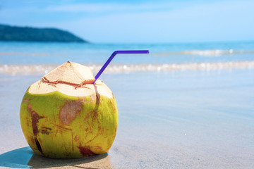 Green coconut water drink with straw on tropical sandy beach