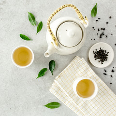 Herbal tea with two white tea cups and teapot, with green tea leaves. Flat lay, top view. Tea concept