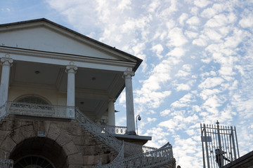  View from the bottom of the stairs with openwork railings leading to the gallery of Catherine Park with columns and arched arches against a blue sky with clouds.