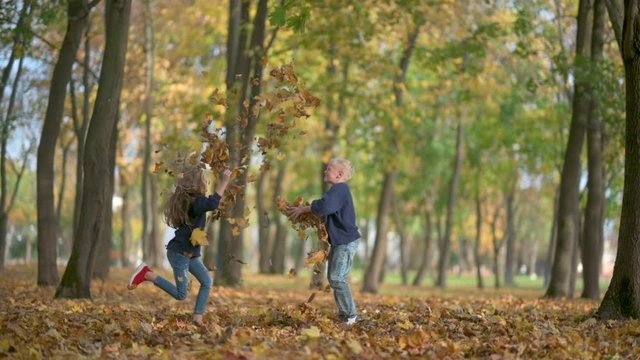 Happy Children Play in the Autumn Park. Boy and Girl Throw and Play a Fallen Leaf Slow Motion. Kids Have Fun in the Outdoors. Childhood Concept.