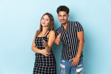 Teenager caucasian couple isolated on blue background shaking hands for closing a good deal