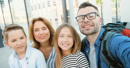 POV of young Caucasian happy family with small teens kids having videochat, smiling and waving with hands outdoor. Mother, father and little girl and boy talking to camera as videochatting.