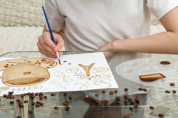 Fototapeta na wymiar Coffee drawings. Girl draws a coffee cup using coffee instead of paints