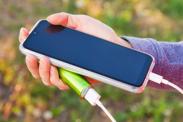 A girl uses a smartphone outdoors while charging from an external power bank