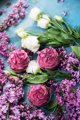 Three pink cupcakes decorated by purple flowers on blue table