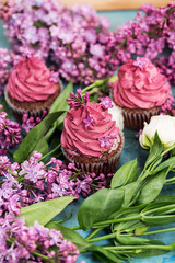 Fototapeta na wymiar Three pink cupcakes with purple lilac and white rose