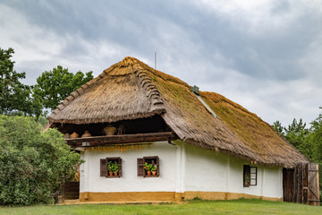 Fototapeta na wymiar Traditional thatched-roofed countryside house with drying corn and blooming pelargonium in Orseg, Hungary.