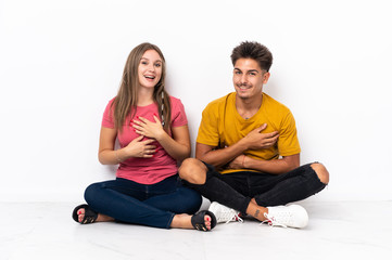 Fototapeta na wymiar Young couple sitting on the floor isolated on white background smiling a lot