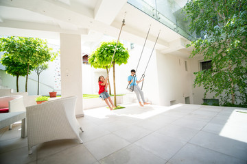 Two kids playing on the swing in a backyard of a villa
