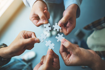 Fototapeta premium Closeup image of a group of people holding and putting a piece of white jigsaw puzzle together