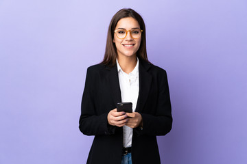 Business woman isolated on purple background sending a message with the mobile